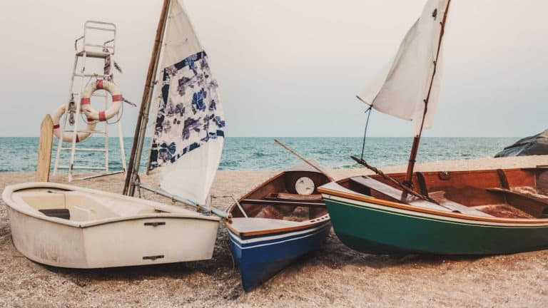Three small sail boats on the shore, sails up